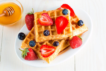Photo of fresh homemade food made of berry Belgian waffles with honey, chocolate, strawberry, blueberry, maple syrup and cream. Healthy dessert breakfast concept with juice. 