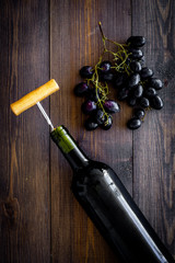 Open the wine concept. Corkscrew into cork of red wine bottle near bunch of grapes on dark wooden background top view copy space