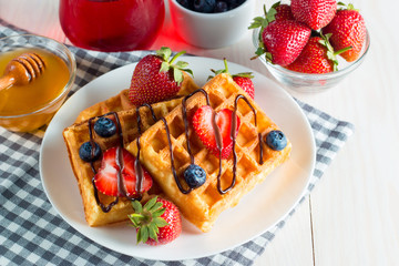 Photo of fresh homemade food made of berry Belgian waffles with honey, chocolate, strawberry, blueberry, maple syrup and cream. Healthy dessert breakfast concept with juice. 