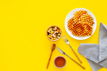 Hot round waffles ready to eat. Belgian recipe. Waffles on plate near honey and dried fruits on yellow background top view copy space