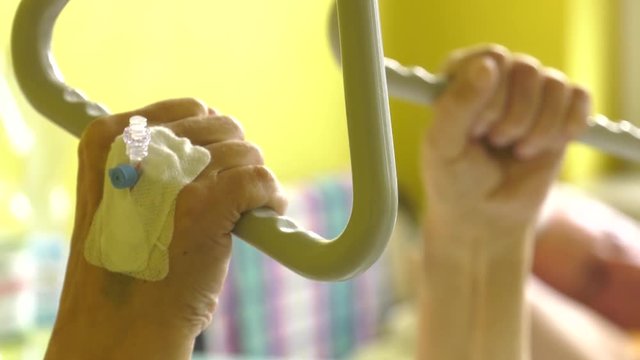 A Very Old Man Lies On A Medical Bed In The Hospital. He Pulls His Hand On A Special Lift.The Hand Has A Peripheral Venous Catheter Panning Camera, Pan, Closeup