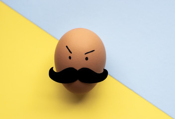 Egg with mustache on light blue & yellow background for Movember concept, an annual event involving the growing of moustaches during the month of November to raise awareness of men's health issues.