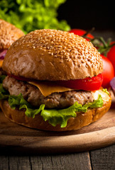 Close-up photo of home made hamburger with beer made of beef, onion, tomato, lettuce, cheese and spices. Fresh burger closeup on wooden rustic table with potato fries and chips.