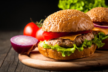 Close-up photo of home made hamburger with beer made of beef, onion, tomato, lettuce, cheese and spices. Fresh burger closeup on wooden rustic table with potato fries and chips.