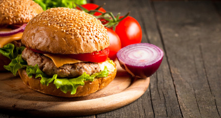 Close-up photo of home made hamburger with beer made of beef, onion, tomato, lettuce, cheese and spices. Fresh burger closeup on wooden rustic table with potato fries and chips.