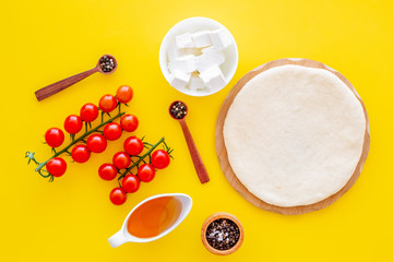 Ingredients for cooking vegetarian pizza. Rolled pizza dough, cherry tomatoes, olive oil, cheese mozzarella, spices on yellow background top view mockup