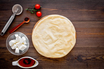 Process of cooking pizza. Pizza Margarita. Raw dough and filling. Cherry tomatoes, cheese mozzarella, spices near knife for pizza on dark wooden background top view mockup copy space