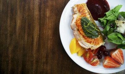 Top view of closeup grilled salmon steak with salad and strawberry sauce on a dark wooden table with copy space for text, organic and healthy eating concept, well-being