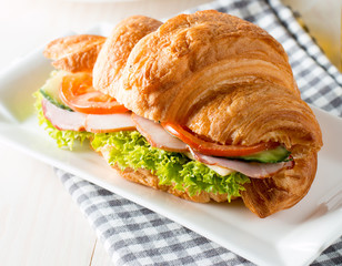 Fresh croissant or sandwich with salad, ham, jamon, prosciutto, salami, cheese, chicken, tomatoes on wooden background. Morning breakfast concept. Healthy and fast food.
