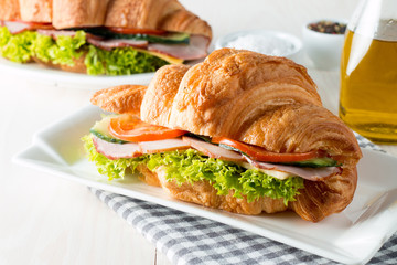 Fresh croissant or sandwich with salad, ham, jamon, prosciutto, salami, cheese, chicken, tomatoes on wooden background. Morning breakfast concept. Healthy and fast food.