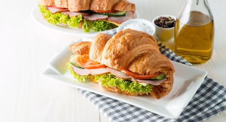 Fresh croissant or sandwich with salad, ham, jamon, prosciutto, salami, cheese, chicken, tomatoes on wooden background. Morning breakfast concept. Healthy and fast food.