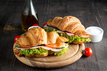 Fresh croissant or sandwich with salad, ham, jamon, prosciutto, salami, cheese, chicken, tomatoes on wooden background. Morning breakfast concept. Healthy and fast food.