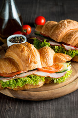Fresh croissant or sandwich with salad, ham, jamon, prosciutto, salami, cheese, chicken, tomatoes on wooden background. Morning breakfast concept. Healthy and fast food.