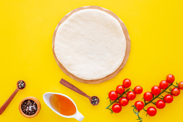 Ingredients for cooking vegetarian pizza. Rolled pizza dough, cherry tomatoes, olive oil, cheese mozzarella, spices on yellow background top view mockup copy space