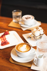 Hot latte coffee and cakes on the wooden table in the cafe.