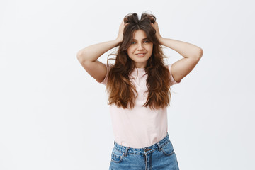Fototapeta premium Indoor shot of happy and carefree woman feeling satisfied after vising hairdresser making incredible hair mask touching fluffy and beautiful hairstyle smiling broadly over gray background