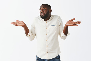 Bro have no idea. Portrait of clueless handsome African American in white shirt and jeans, shrugging with both hands aside, pursing lips and pouting, being unaware and uncertain in answer