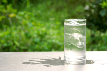 Glass of ice and water in put on table in the nature green background