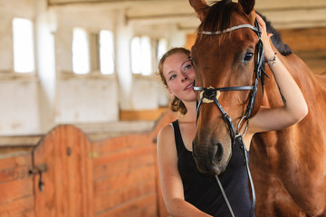 Jockey young girl petting and hugging brown horse