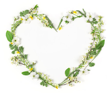 Heart symbol made of spring flowers and leaves isolated on white background. Flat lay. Top view.