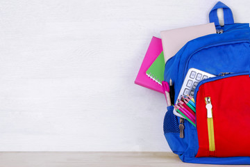 A school backpack with various school supplies on a white wooden background with a place for an inscription