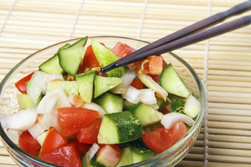 Healthy breakfast or dinner from natural organic cucumbers, tomatoes and onion on bamboo mat. Chinese or japanese kitchen concept. Copy space