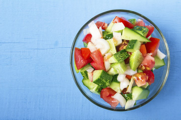 Chopped vegetables - cucumbers, tomatoes and onions in glass bowl on wooden table. View from above. Copy space