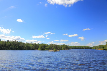Gorgeous nature landscape view of lake with rocky coast line and green tall trees on blue sky...