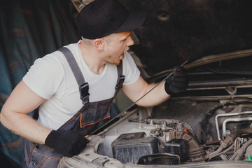 Car mechanic working diagnostic equipment at automotive service. Checking oil level.