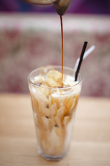 Barista prepares summer cold coffee with ice and milk in transparent glass.