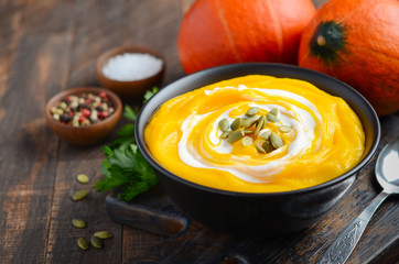 Pumpkin cream soup with cream and pumpkin seeds on rustic wooden table.