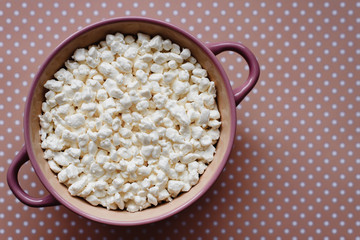 Cottage cheese in a ceramic bowl on a pink background in polka dots, homemade rural healthy food