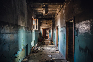 Dirty empty dark corridor in burned abandoned building after fire, broken doors, garbage, perspective