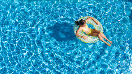 Aerial top view of little girl in swimming pool from above, kid swims on inflatable ring donut , child has fun in blue water on family vacation resort
