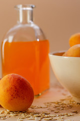 Lots of apricots on a white plate and glass of apricot juice on a white table strewn with oatmeal.