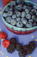 Fresh berries. Blueberries in a plate and blackberries and raspberries on a blue background. Summer harvest.