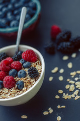 Healthy breakfast. White plate with oatmeal strewn and different berries on a blue background. Summer harvest.