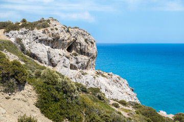 Greek scenery - cave in a rocky mountain with green bushes  on a coastline.