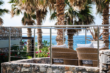 View from behind on empty rattan chairs on a resort's balcony facing the sea.