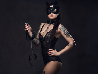 Fototapeta na wymiar Sexy woman wearing black lingerie in BDSM cat leather mask and accessories posing on dark background. 