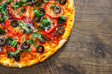 Pizza with Mozzarella cheese, salami, pepper, pepperoni, Tomatoes, olives, Spices and Fresh Basil. Italian pizza on wooden background. with copy space. top view