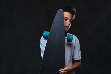Portrait of a young skater boy dressed in a white t-shirt holds a longboard. Isolated on the dark background. © Fxquadro