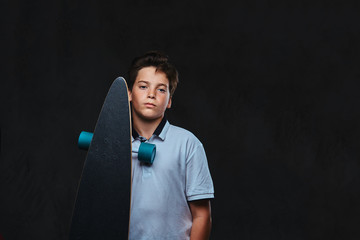 Portrait of a young skater boy dressed in a white t-shirt holds a longboard. Isolated on the dark background. © Fxquadro
