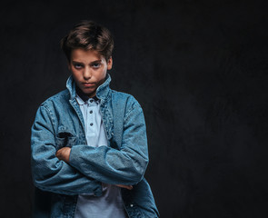 Fashionable young guy dressed in a t-shirt and denim jacket posing with crossed arms in a studio.