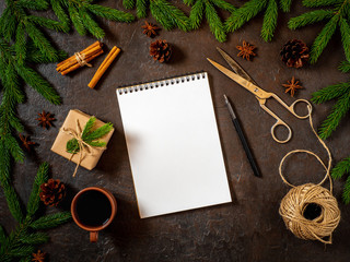 Empty white notebook and pen on dark black Christmas background of fir branches, cones, gifts. Letter, mock up