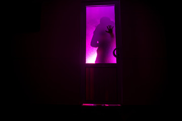 Silhouette of an unknown shadow figure on a door through a closed glass door. The silhouette of a human in front of a window at night. Scary scene halloween concept