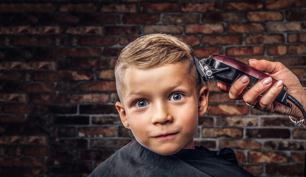 Close-up portrait of a cute smiling boy getting haircut against a brick wall.