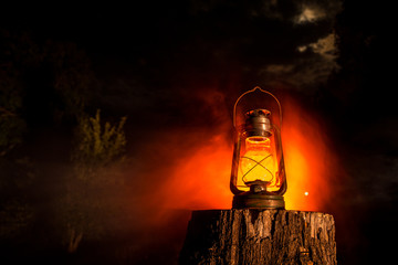 Horror Halloween concept. Burning old oil lamp in forest at night. Night scenery of a nightmare...