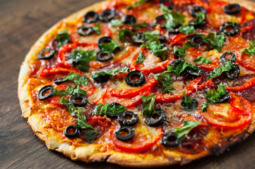 Pizza with Mozzarella cheese, salami, pepper, pepperoni, Tomatoes, olives, Spices and Fresh Basil. Italian pizza on wooden background