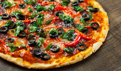 Pizza with Mozzarella cheese, salami, pepper, pepperoni, Tomatoes, olives, Spices and Fresh Basil. Italian pizza on wooden background